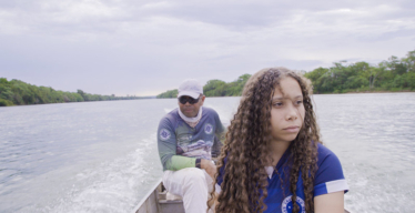 Duas pessoas em um barco, um homem no fundo e uma adolescente em primeiro plano.