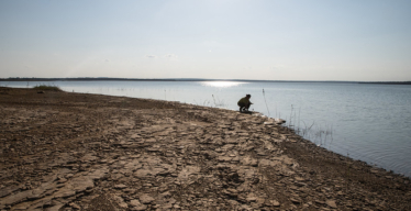 Imagem de pessoa ao longe agachada à beira de espelho d'água.