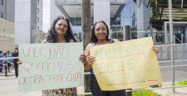 Duas mulheres seguram cartazes exigindo reparação pelo desastre da Vale em frente ao Tribunal de Justiça em Belo Horizonte