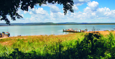 Imagem de ambiente aberto, com margem de represa e porto.
