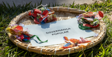 Foto de uma peneira de palha com papel escrito "governança popular" e enfeites. Foto de Daniela Paoliello.