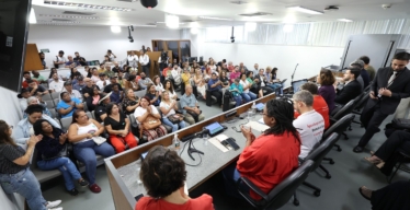 Auditório cheio, com pessoas sentadas e em pé. O público que está assistindo aparece de frente e as pessoas que compõem a mesa do evento de costas. Foto: Luiz Santana/ALMG