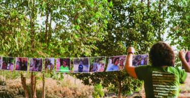 Mulher de costas utilizando o uniforme do Instituto Guaicuy em ambiente aberto pendura foto em varal.