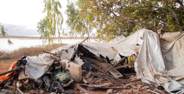 Destroços de construção e itens pessoais danificados próximos a vegetação e represa