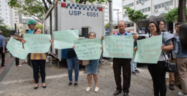 Dois homens e quatro mulheres seguram cartazes com pedidos de direitos como o auxílio emergencial e a reparação.