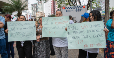 Pessoas atingidas mostram cartazes em defesa de auxílio emergencial em manifestação (foto de Fabiano Lana).