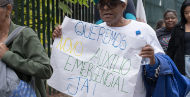 Homem com óculos e boné do MAB exibe cartaz exigindo o Novo Auxílio Emergencial (acervo Guaicuy).