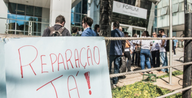 Cartaz de pessoa atingida diz "reparação já!" em frente ao Fórum