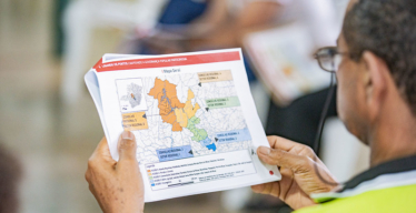 Homem segura material impresso com o mapa das cincos regiões atingidas e a localização dos Conselhos e Setores Regionais.