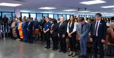 Auditório cheio de pessoas vestidas com roupas formais. Na primeira fila, três delas utilizam uniformes: Polícia Militar, Defesa Civil e Corpo de Bombeiros de Minas Gerais. No canto esquerdo da imagem há profissionais da imprensa registrando o evento.