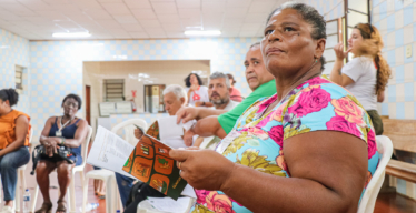 Mulher negra olha para a frente, com o Almanaque de Projetos da Região 4 nas mãos, durante atividade do Anexo 1.1 - Acervo Guaicuy.